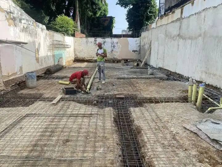 Patio de obra con losa, armadura y cuadrilla en un predio industrial
